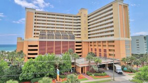 Ein mehrstöckiges Hotel mit einem zentralen Atrium, Parkplätzen im Freien und Meerblick.