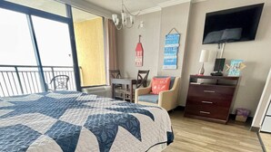 Ein Hotelzimmer mit einem großen Bett, einem Schreibtisch mit Stuhl, einem Fernseher und einem Balkon mit Aussicht.