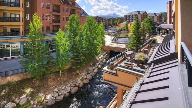 A multi-story hotel with balconies, a river running through the courtyard, and a mountainous backdrop.