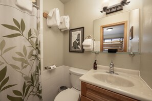 A bathroom with a toilet, sink, and shower curtain. There is a framed picture on the wall and a towel rack with towels.
