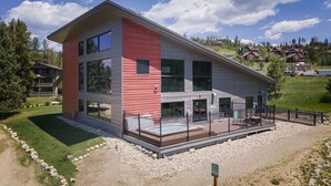 A modern two-story house with a red and white exterior, a fenced patio, and a clear view of the surrounding landscape.