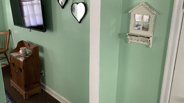 A room with a green wall, a wooden cabinet, a television, and a small white shelf with a mirror. - Beach Side Studio #1 Apts by RedAwning (Norfolk)
