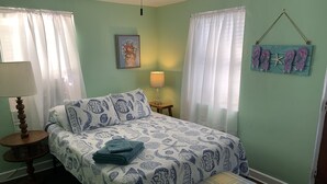 A bedroom with a bed, a nightstand, a lamp, a framed picture on the wall, and a wall decoration of flip-flops and a starfish. - Beach Side Studio #1 Apts by RedAwning (Norfolk)