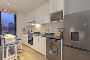 A modern kitchen with stainless steel appliances, white cabinetry, and a large window offering a city view. - The Tokyo 1508 (Cape Town)