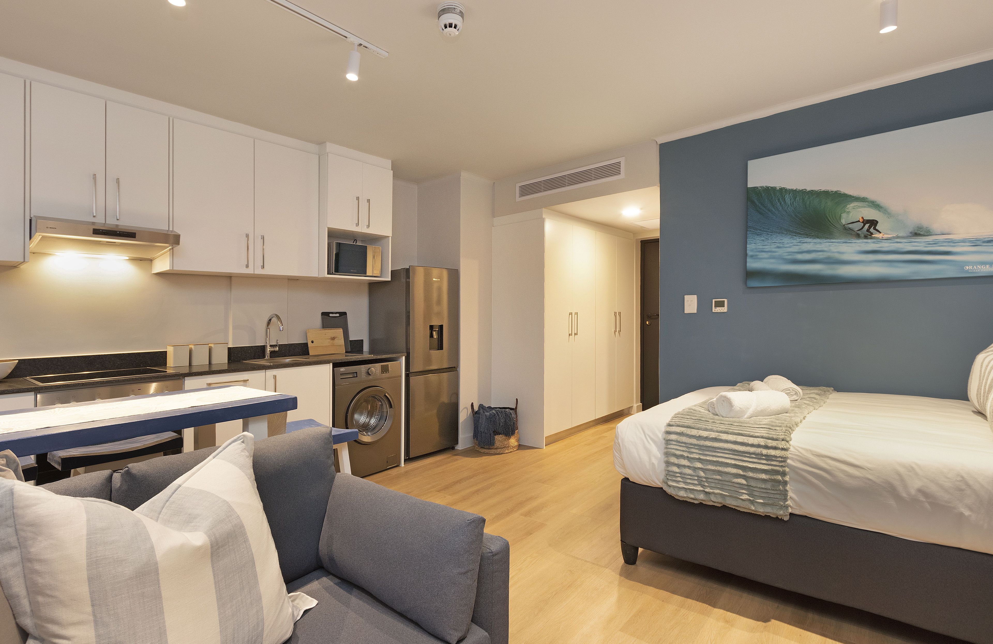 Una habitación de hotel moderna con kitchenette, una cama con vistas a la playa y un ventanal grande.