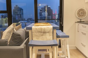 A modern kitchen with a city view, featuring a bar stool, a cushioned bench, and a dining table. - The Tokyo 1508 (Cape Town)
