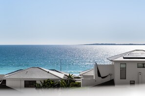 A coastal view with a clear sky, a body of water, and a white building with a sloped roof. - Coral Island 204 (Cape Town)