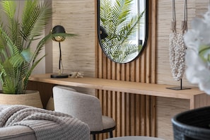 Un intérieur moderne avec un mur lambrissé en bois, un miroir rond, un lampadaire noir et une plante en pot.