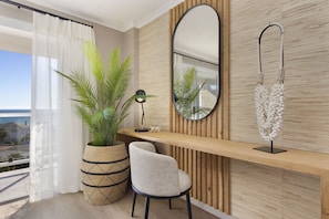 A modern room with a large window, a potted plant, a desk, a chair, a mirror, and a wall-mounted light fixture. - Coral Island 204 (Cape Town)