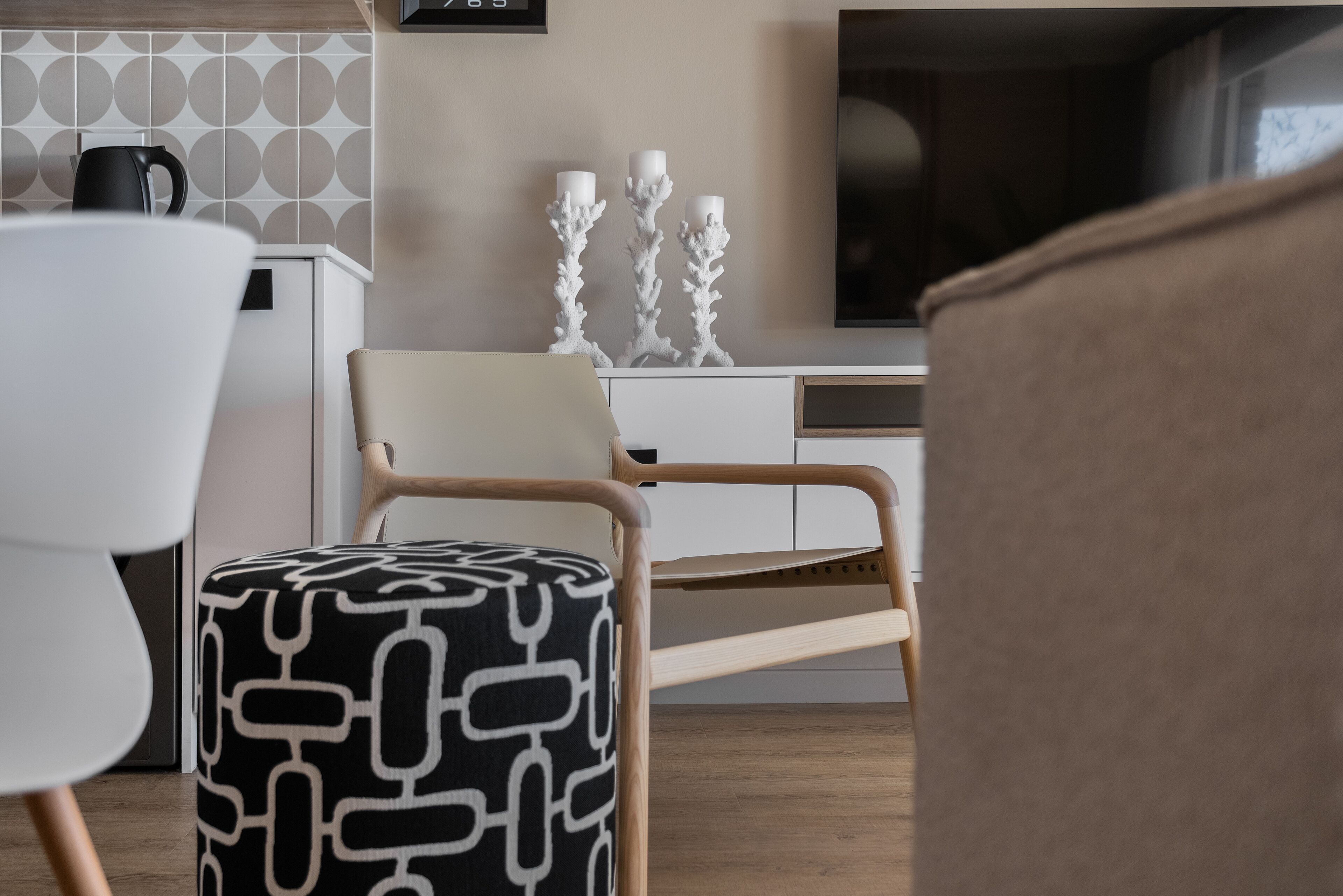 A modern living room with a wooden chair, a patterned ottoman, and a white sofa.