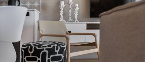 A modern living room with a wooden chair, a patterned ottoman, and a white sofa.
