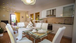 Une cuisine moderne avec des meubles blancs, une hotte en acier inoxydable et un coin repas comprenant une table en verre et des chaises blanches.
