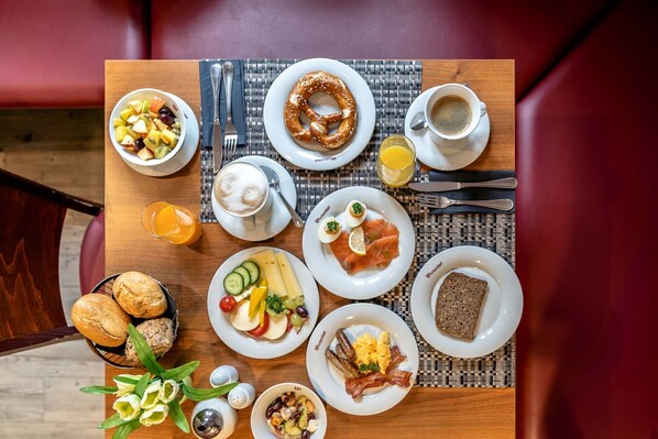 Una mesa de desayuno con diferentes platos, incluyendo un pretzel, café y un plato con huevos y tocino.