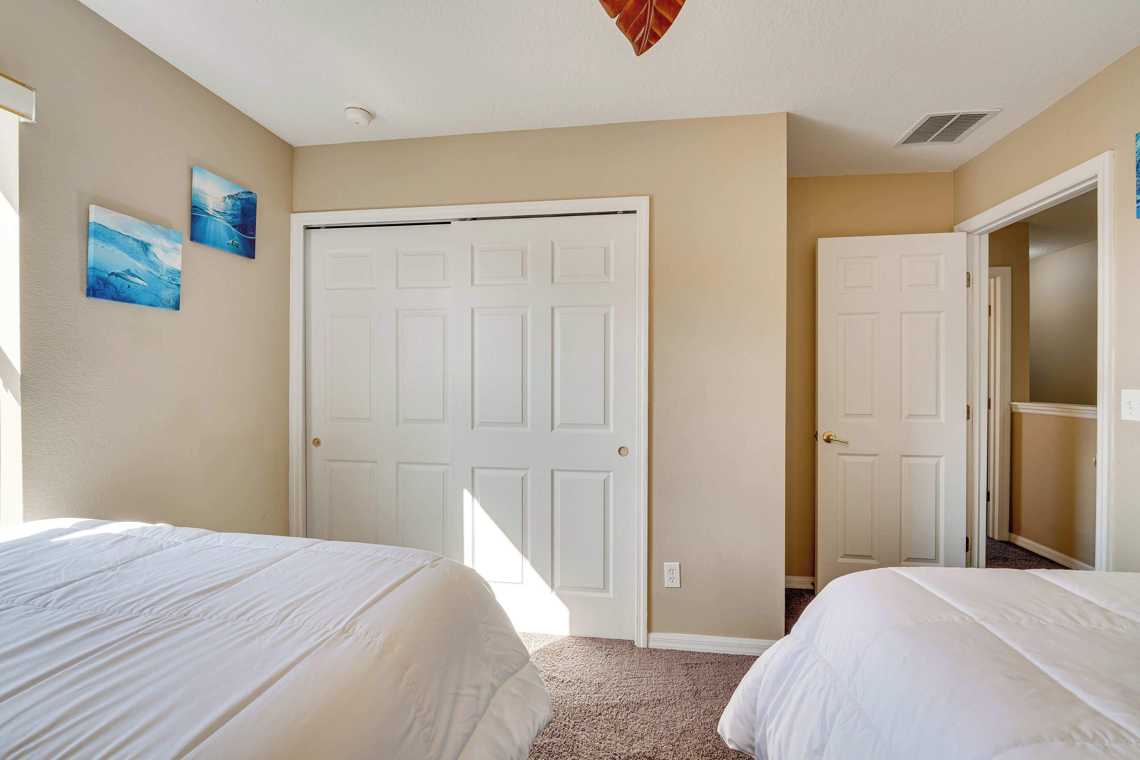 A bedroom with two beds, a white door, and two wall-mounted paintings.