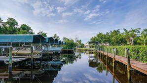 A calm waterway with docks and boats, surrounded by lush greenery and a clear sky. - Fort Myers Getaway w/ Hendry Creek Access! (Fort Myers)