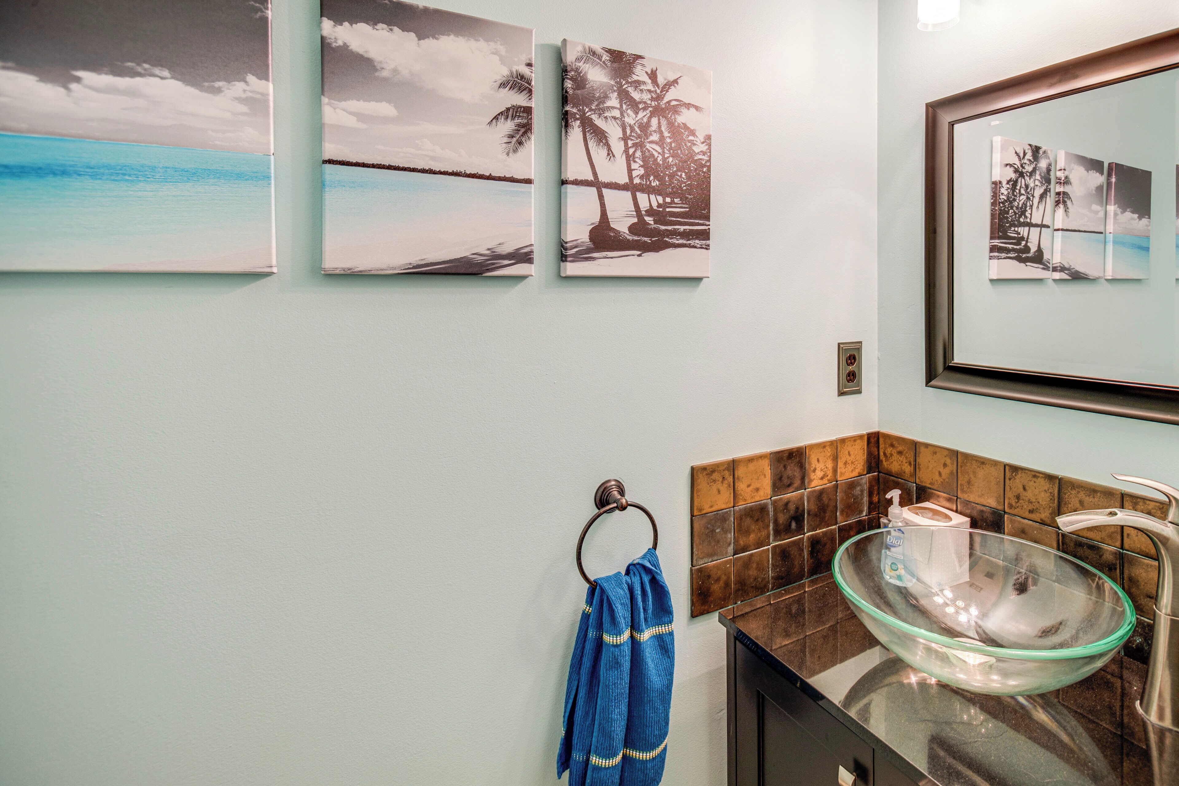 A bathroom with a glass bowl sink, a towel rack with a blue towel, and three framed pictures on the wall.
