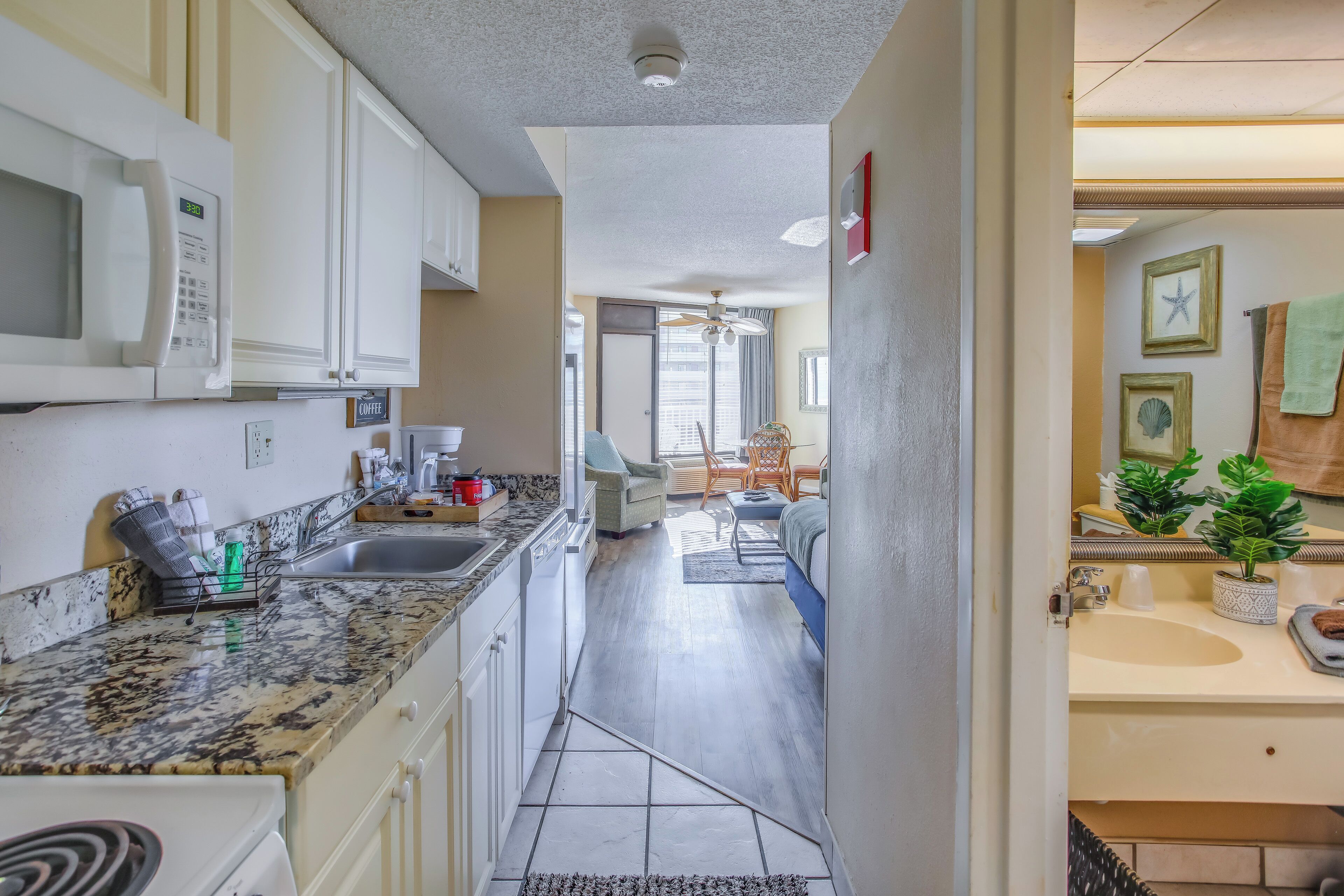 A kitchen with a microwave, sink, and granite countertop. There is a dining area with a chair and a table.