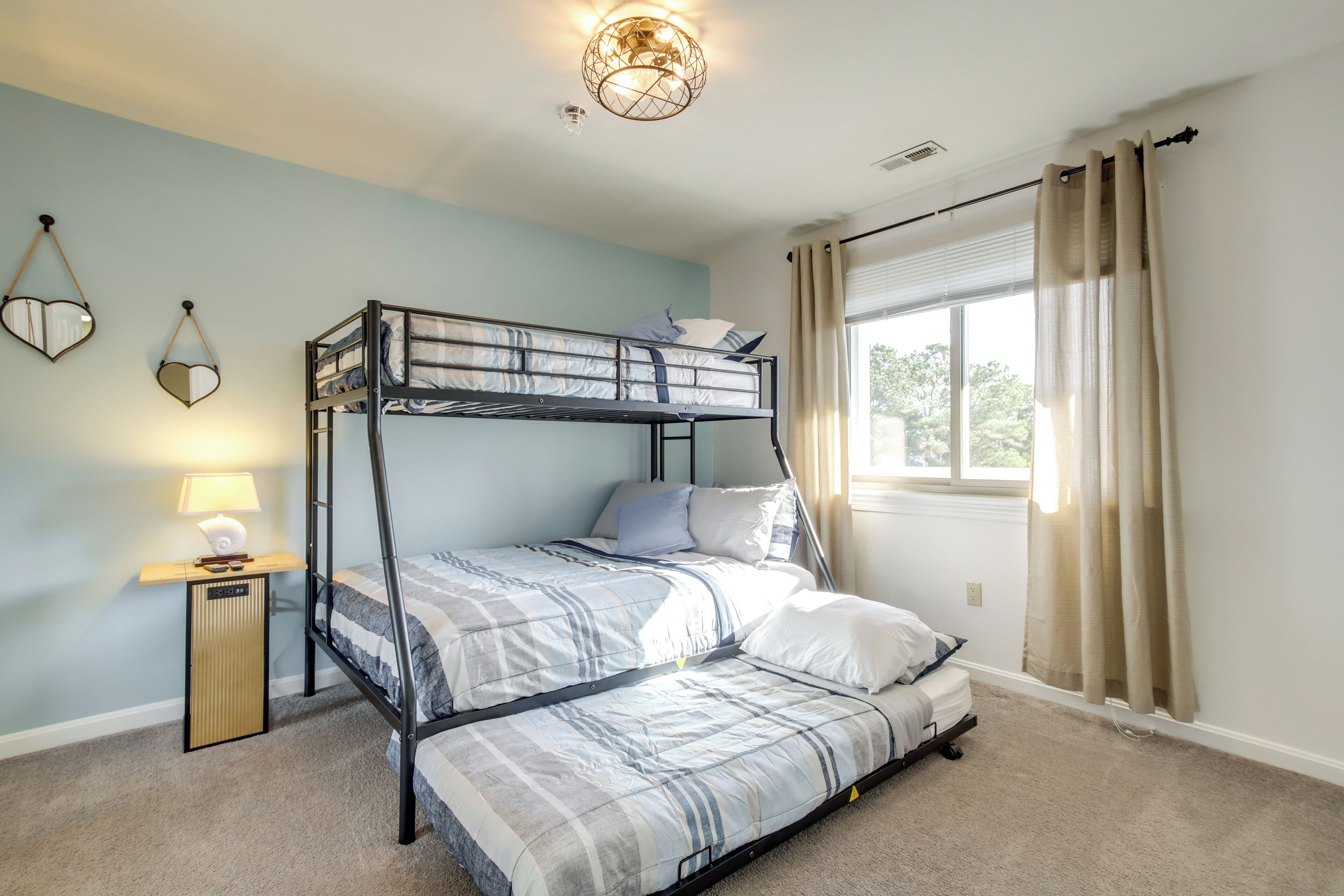A bunk bed room with a nightstand, lamp, and window with curtains.
