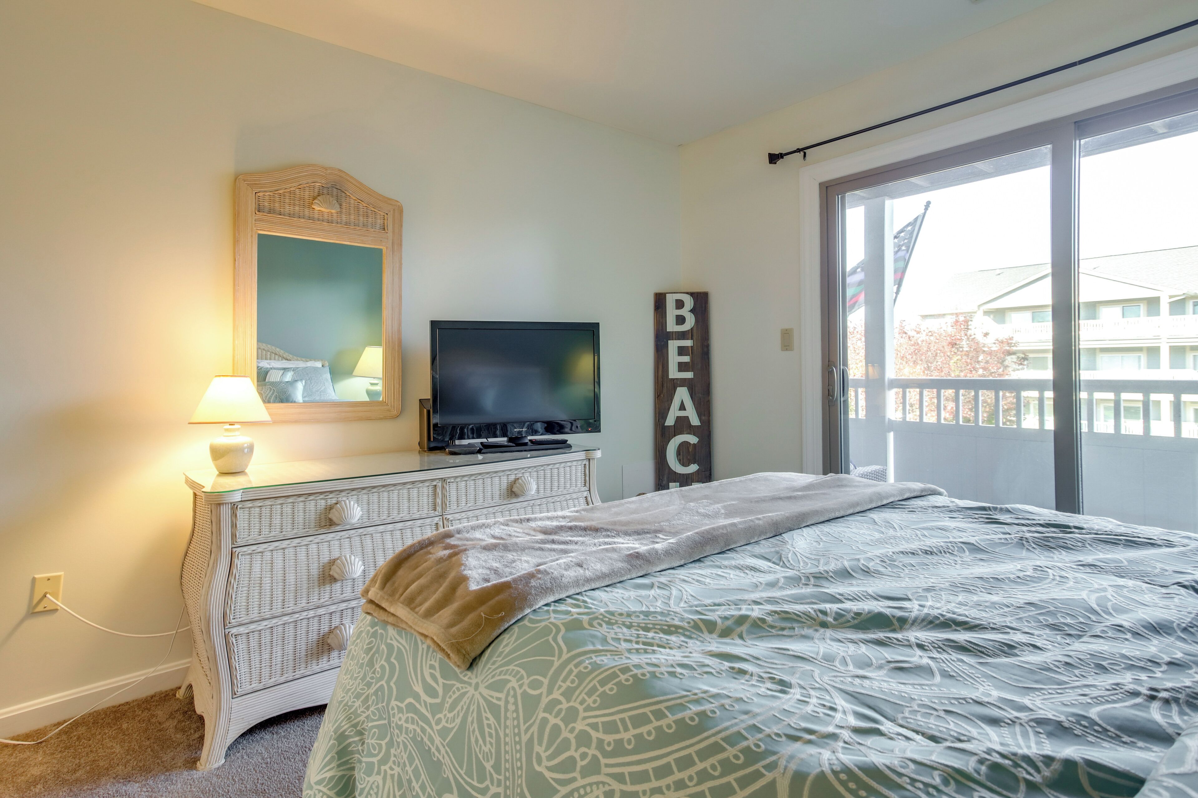 Une chambre à coucher comprenant un lit, une commode, un téléviseur et une grande fenêtre donnant sur des immeubles.