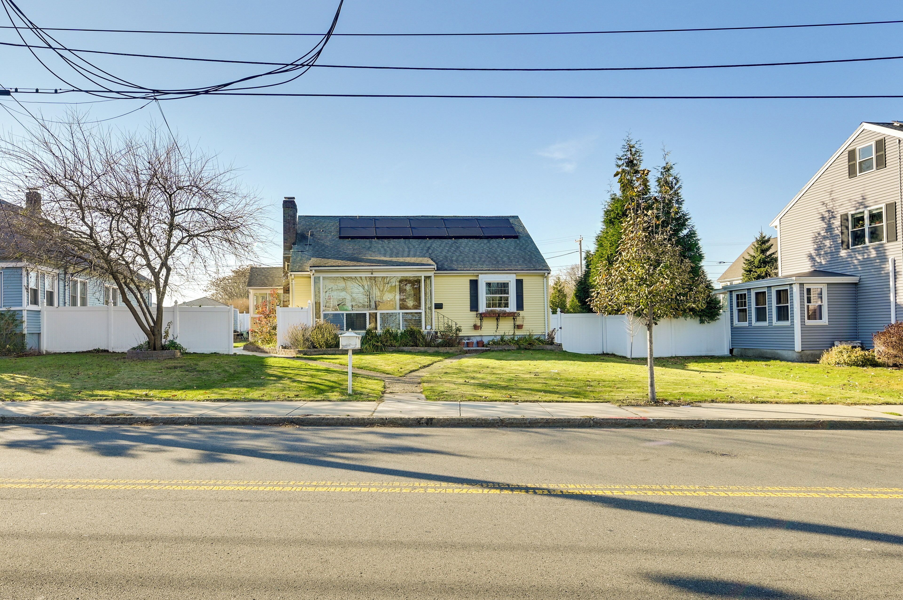 A residential street with houses, a clear sky, and a road with yellow lines.