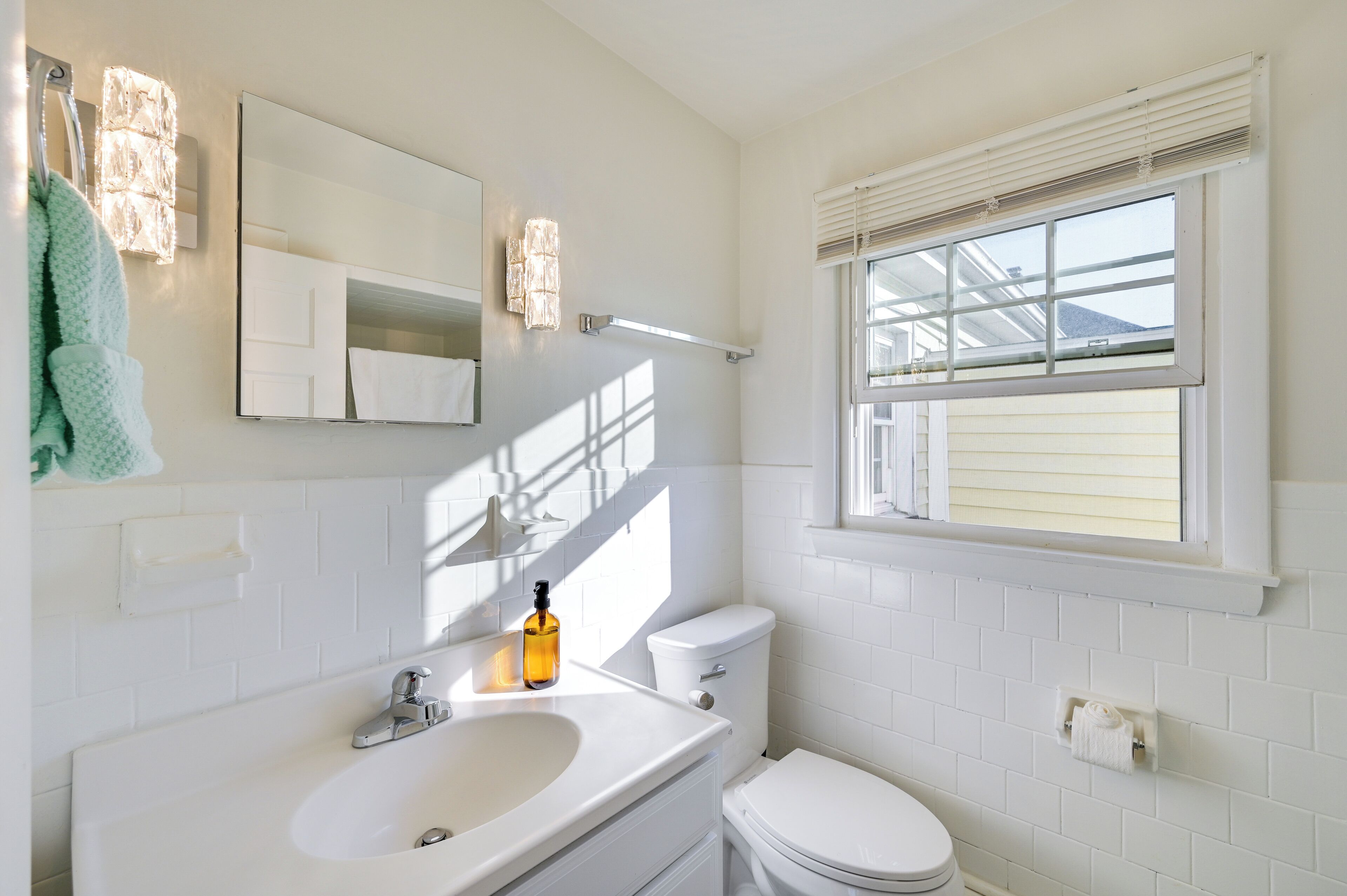 A bathroom with a white sink, toilet, and window with blinds.