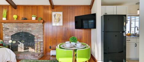 Una sala de estar acogedora con chimenea de ladrillo, una mesa redonda con sillas y un refrigerador negro moderno.