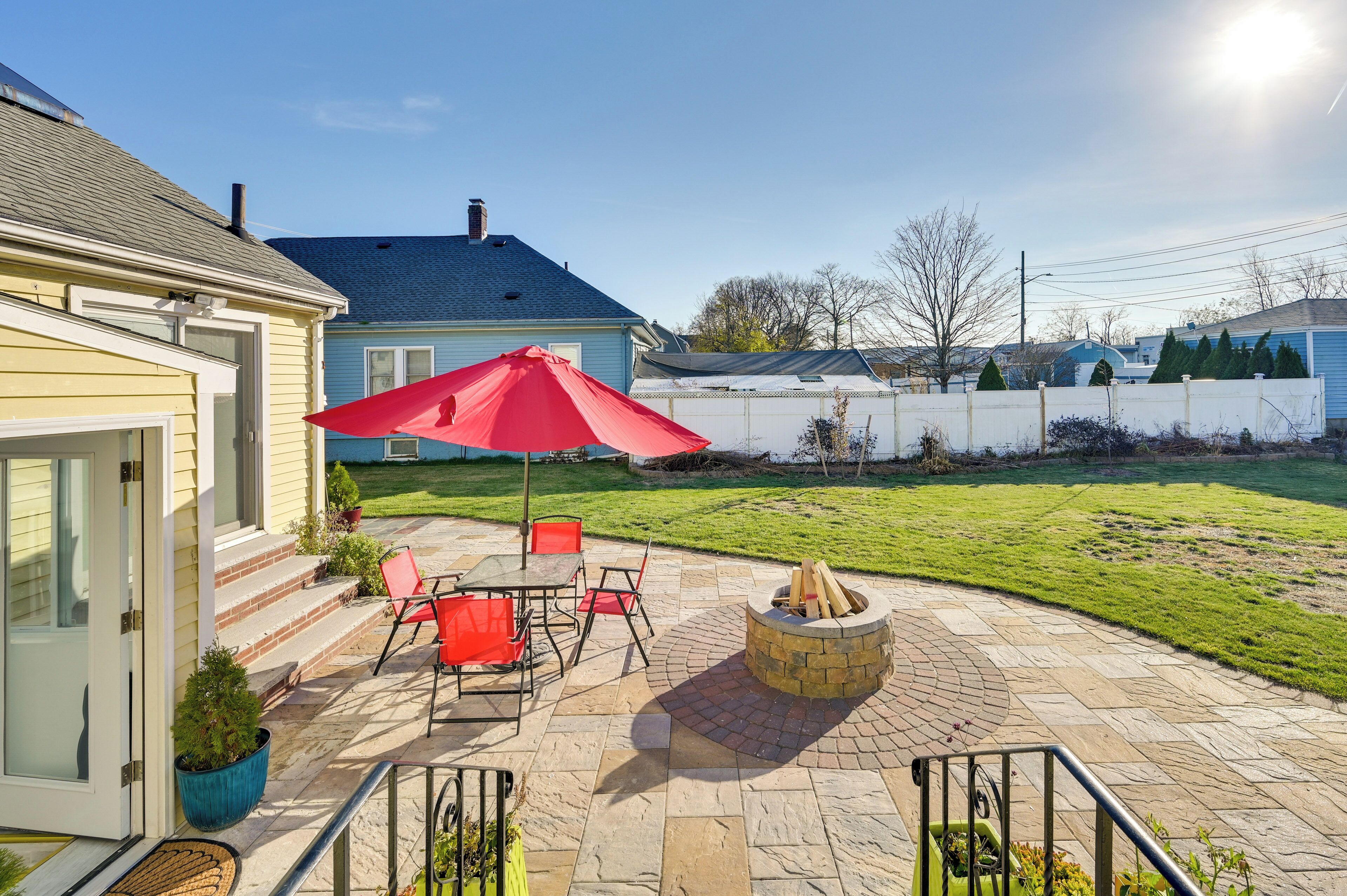 A patio with a fire pit, outdoor furniture, and a red umbrella.