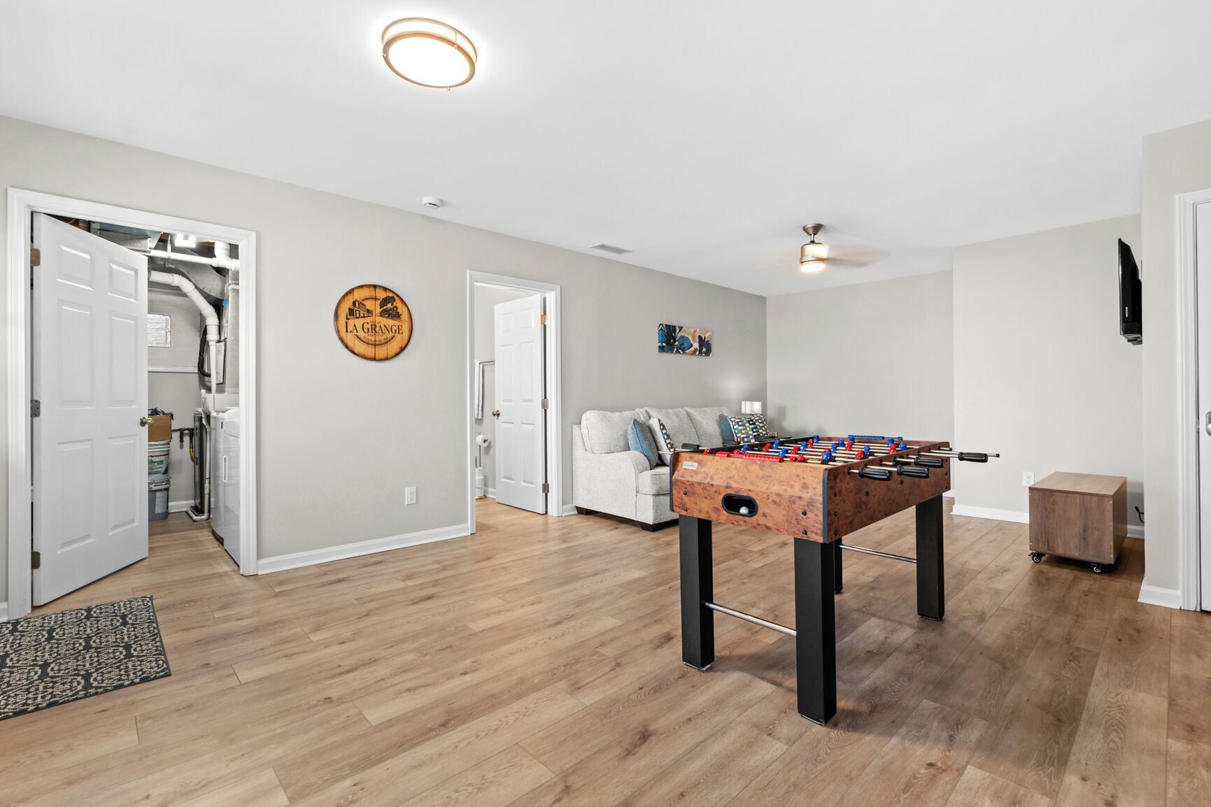 En rummelig stue med et bordfodboldspil, en grå sofa og en loftsvifte.