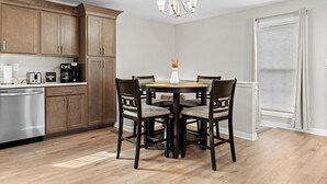 A kitchen with wooden cabinets, a stainless steel dishwasher, a coffee maker, and a dining table with chairs.