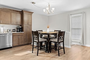 Una cocina con armarios de madera, un lavavajillas de acero inoxidable, una cafetera y una mesa de comedor con sillas.