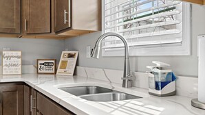 A modern kitchen with two stainless steel sinks, wooden cabinets, a window with blinds, and motivational wall art.