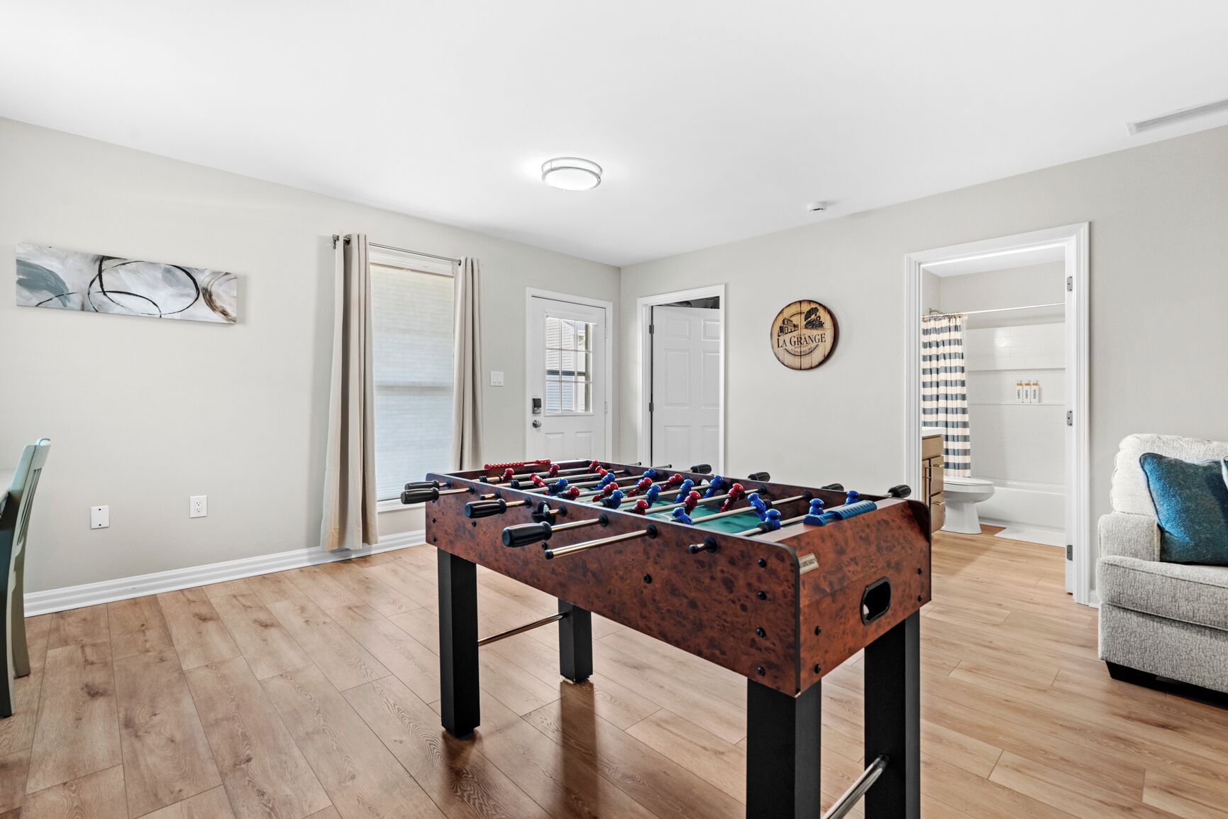 A room with a foosball table, a door, a wall-mounted sign, and a bathroom visible through an open door.