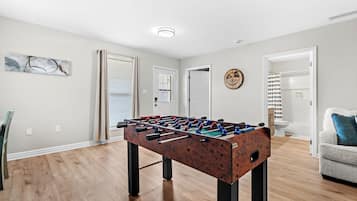 A room with a foosball table, a door, a wall-mounted sign, and a bathroom visible through an open door.