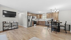 A modern kitchen with wooden cabinets, stainless steel appliances, and a dining area with a chandelier.