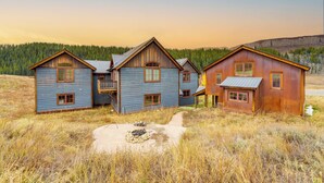A rustic cabin with a large front porch and a fire pit in the yard.