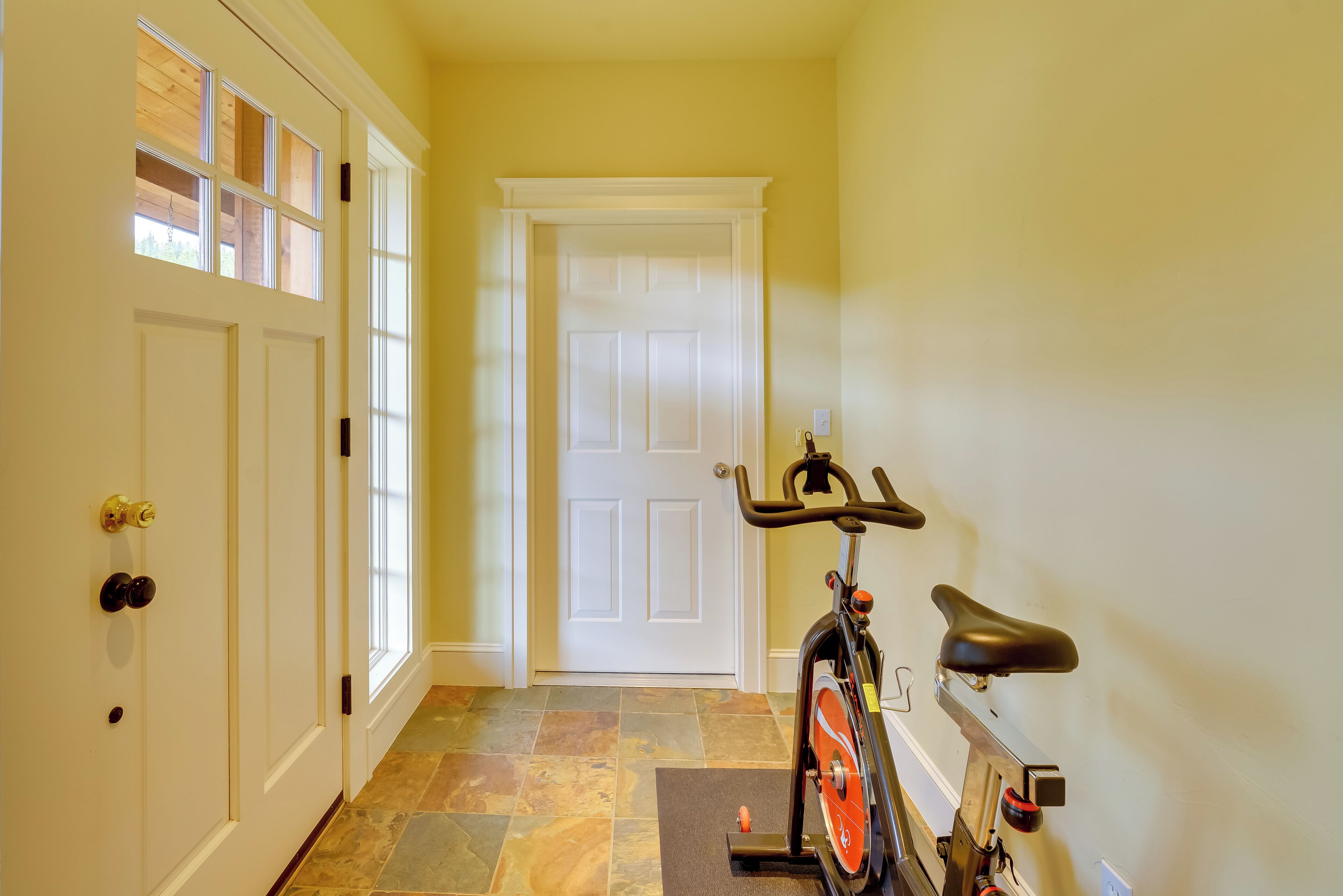 A hallway with a stationary bike, a door, and a window.