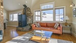 A cozy living room with a stone fireplace, a leather sofa, and large windows offering a snowy view.