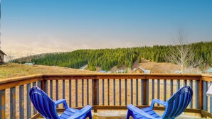 A wooden deck with two blue chairs facing a forested hillside.