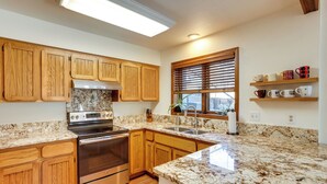A kitchen with wooden cabinets, granite countertops, stainless steel appliances, and a window with blinds. - Near Trails! Sun-drenched Durango Escape w/ View (Durango)