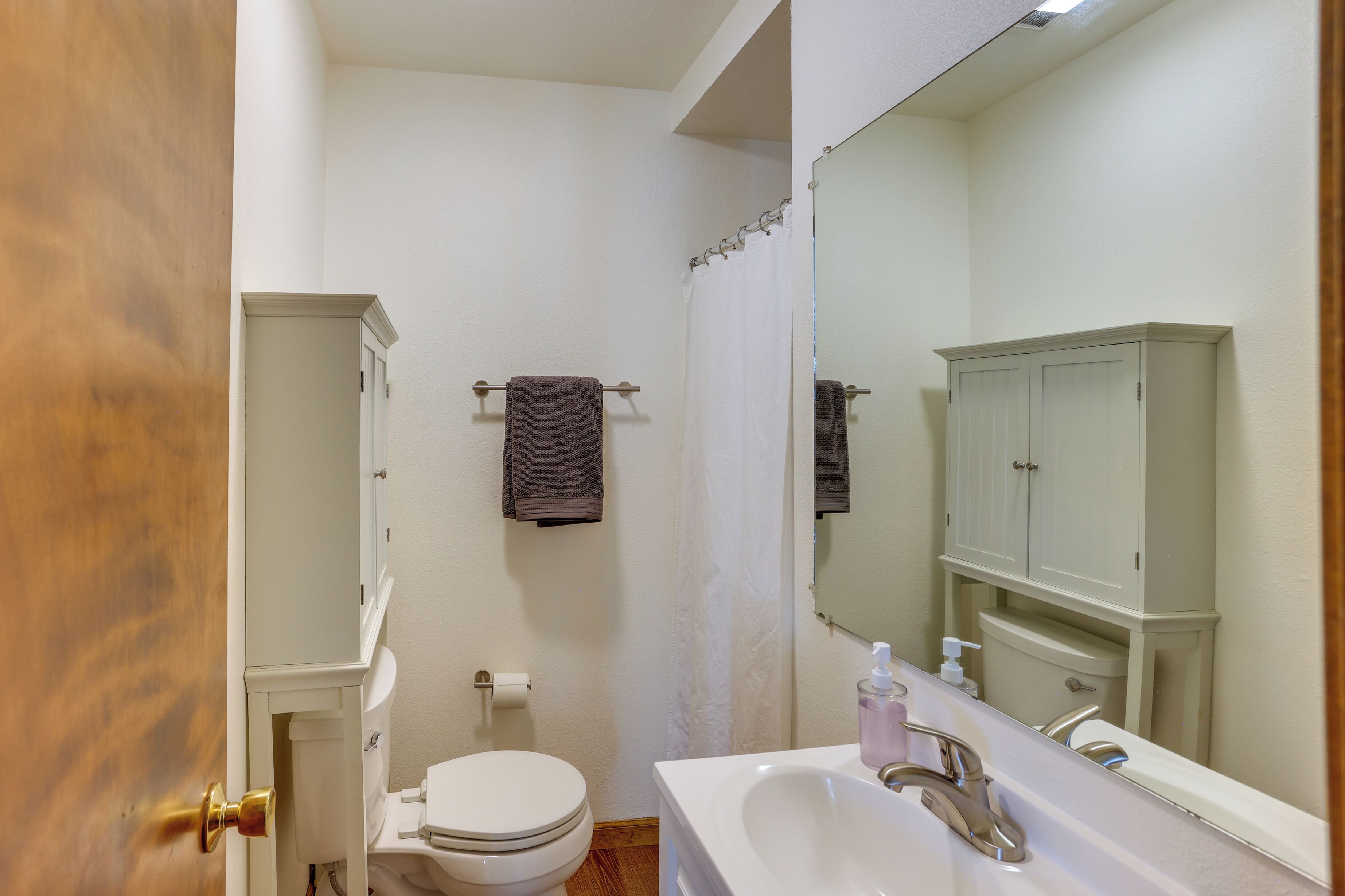 A bathroom with a toilet, sink, mirror, and cabinet.