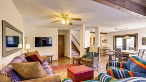 A spacious living room with a ceiling fan, a television, and a dining area with a staircase leading upstairs. - Near Trails! Sun-drenched Durango Escape w/ View (Durango)