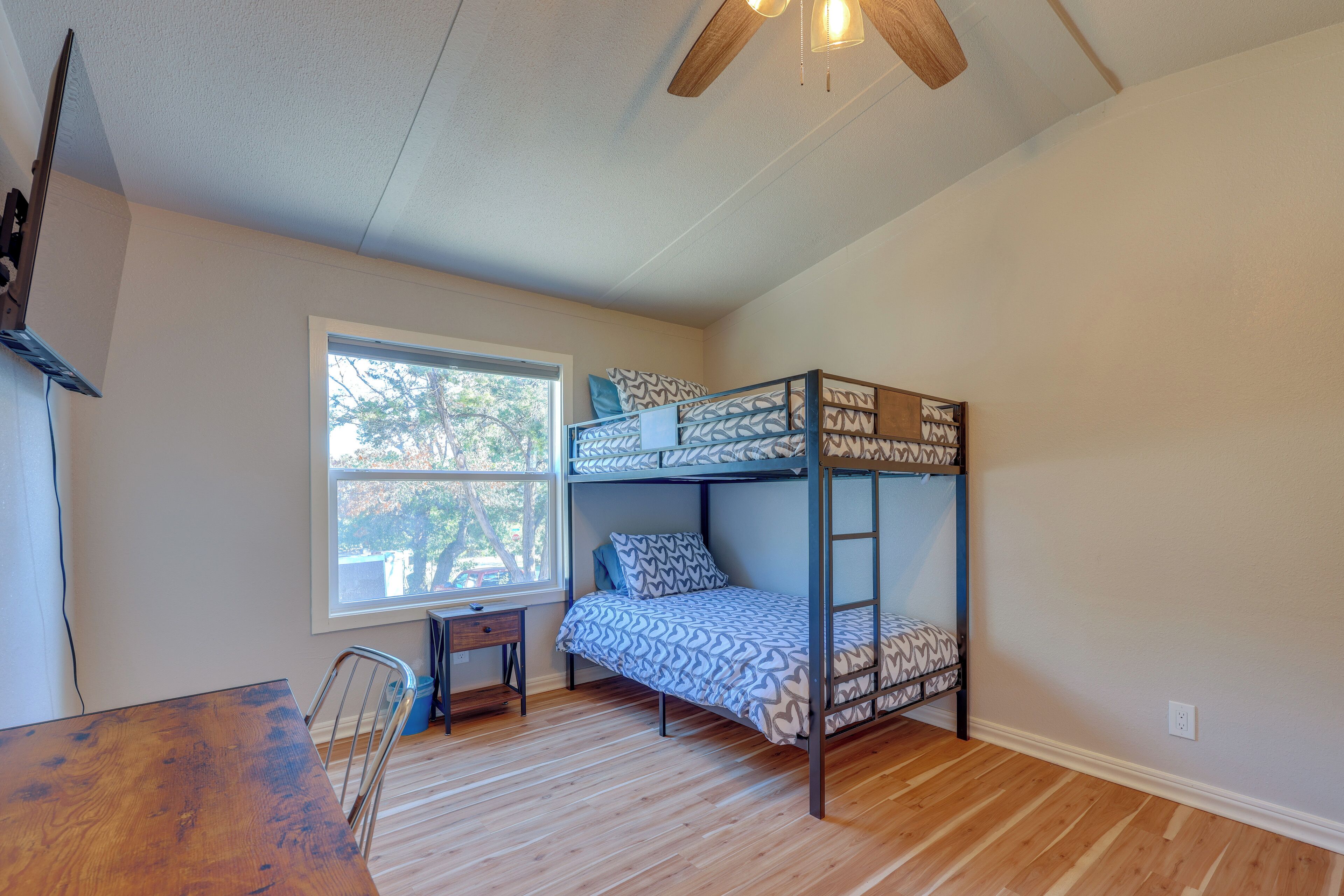 A room with a bunk bed, a desk, a chair, and a window with a view of trees.