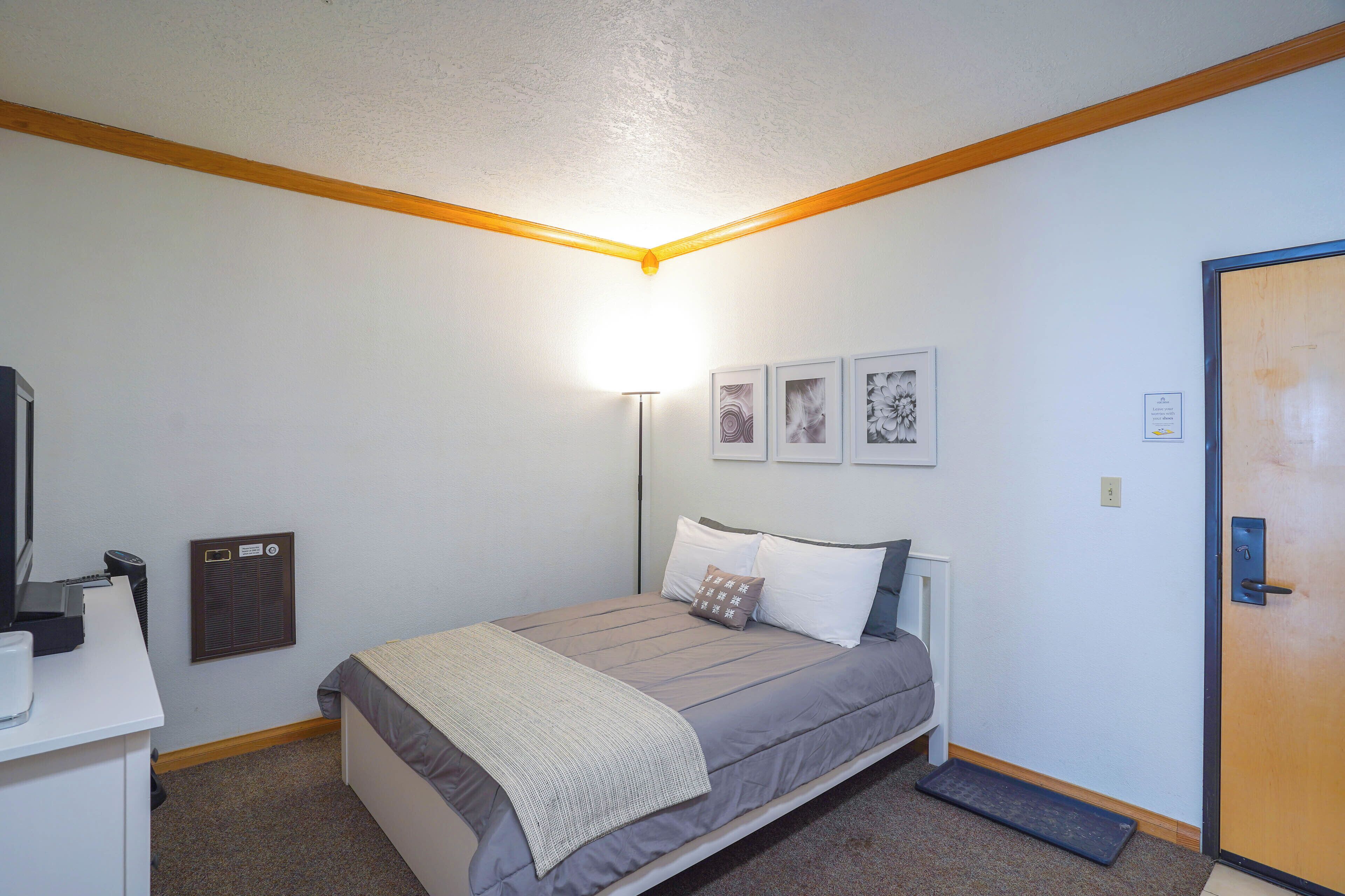 Un dormitorio con cama, mesita de noche, lámpara y cuadros en la pared.