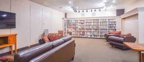 A library with leather sofas, a wooden table, and a bookshelf filled with books.