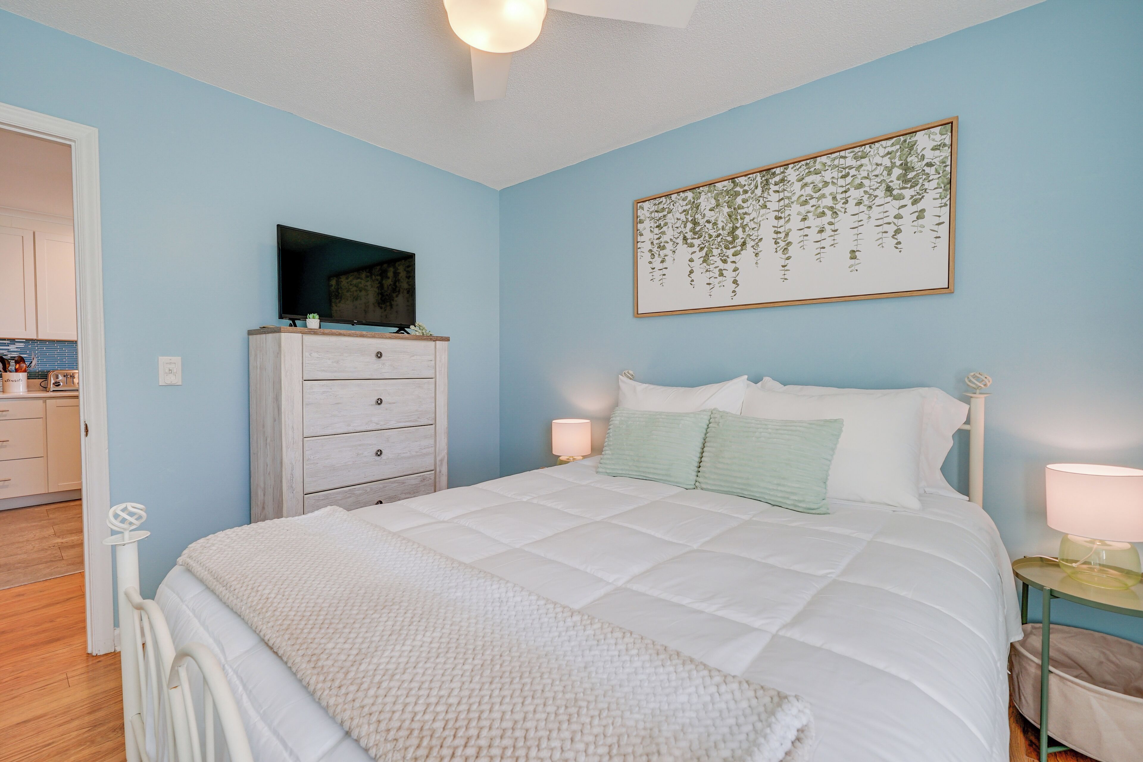A bedroom with a bed, a dresser, a television, and a wall-mounted artwork.