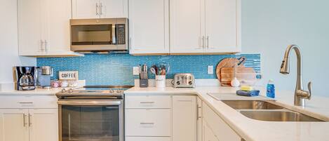 A modern kitchen with white cabinets, a stainless steel oven, a microwave, and a sink.