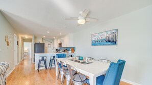 A modern kitchen with white cabinets, a central island, and blue bar stools. - Steps to Ocean: Water-view Carolina Beach Unit! (Carolina Beach)