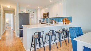 A modern kitchen with white cabinets, a central island with bar stools, a microwave, and a sink. - Steps to Ocean: Water-view Carolina Beach Unit! (Carolina Beach)