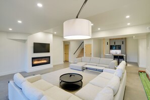 A modern living room with a fireplace, a large sofa, a coffee table, and a kitchen area in the background.