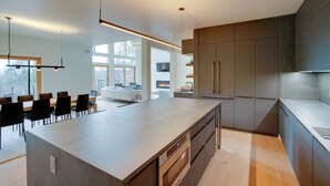 Een moderne keuken met een groot eiland, donkere kastjes en hanglampen.